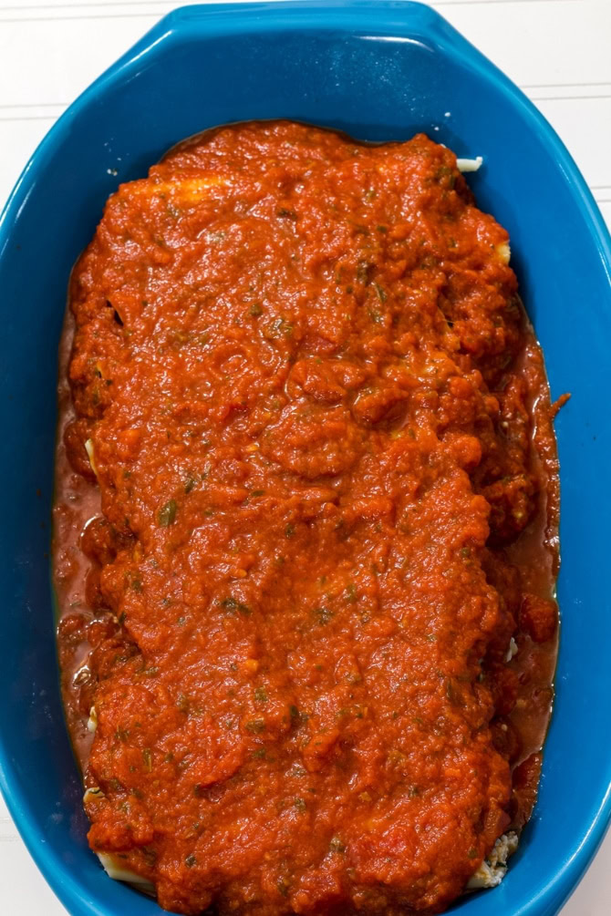 The cheese and spinach manicotti in the casserole dish with sauce on top of it ready to go into the oven.