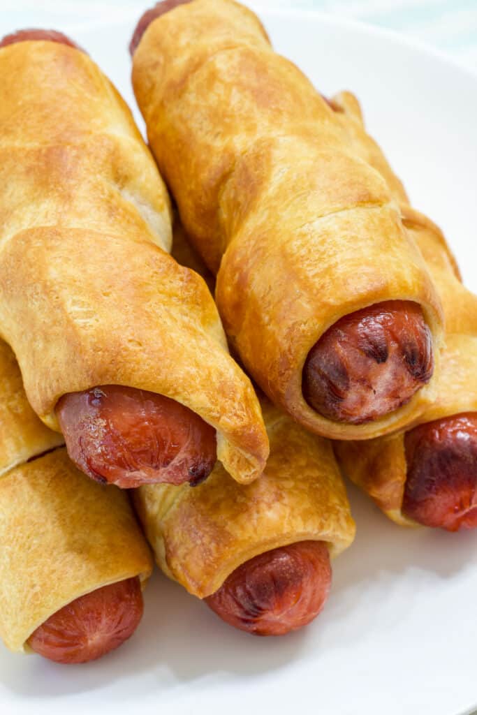 Five Air Fryer Pigs in a Blanket stacked on a plate.