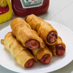 Five pigs in a blanket on a white plate.