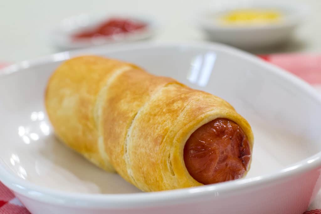 One Air Fryer Pigs in a Blanket on a white plate.