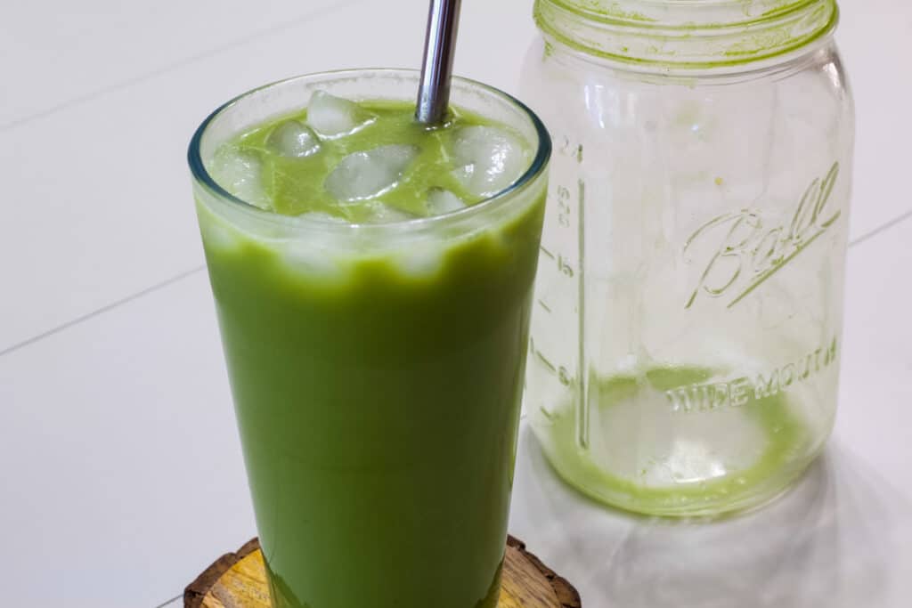 One glass of Copycat Starbucks Iced Pineapple Matcha Drink and an empty mason jar sitting next to it.