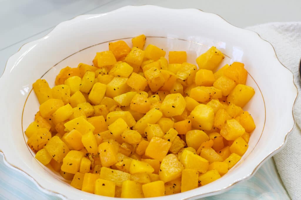 A china serving bowl full of butternut squash after it has been cooked in the air fryer.