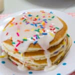 A stack of four confetti pancakes with vanilla icing dripping on them.