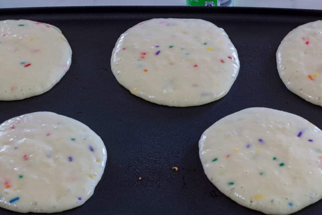 Cake mix funfetti pancakes cooking on an electric griddle pan before they have been flipped over.