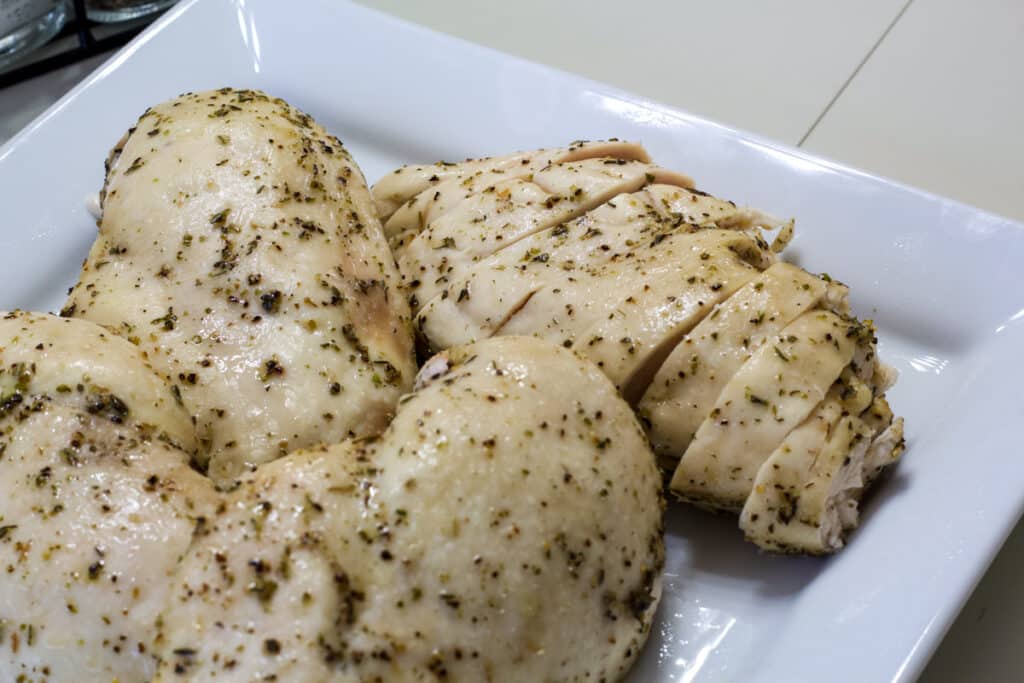 Four cooked chicken breasts on a square white plate, one has been sliced.