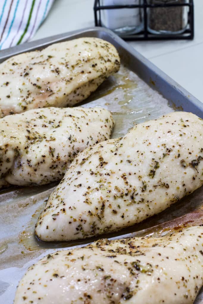 Four cooked chicken breasts on a silver parchment paper lined sheet pan.