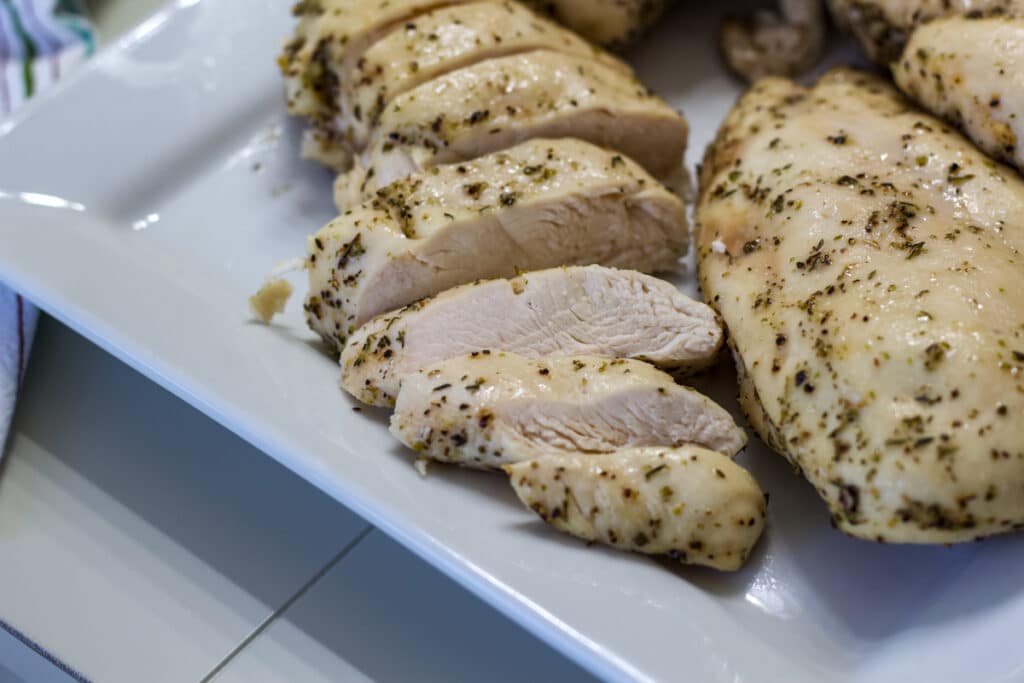 Chicken breasts on a plate, one has been sliced so you can seed the cooked inside.