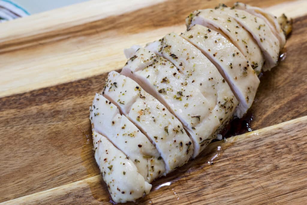 One cooked chicken breast on a wooden cutting board, it has been sliced.