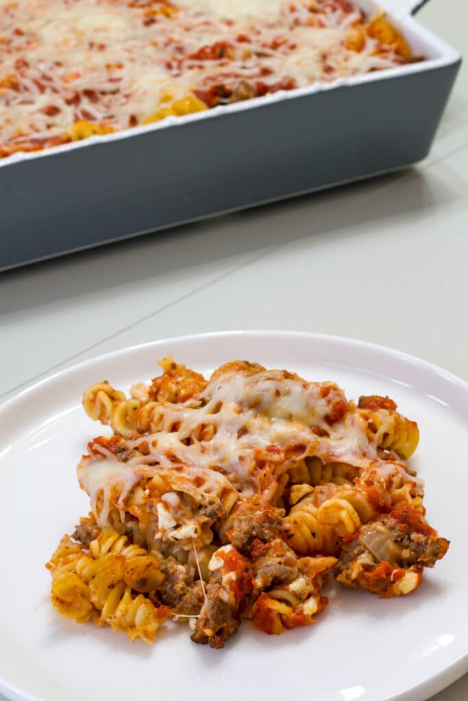 One serving of Quick and Easy Homemade Lasagna Casserole on a plate in the foreground and the remaining pasta casserole in the background.