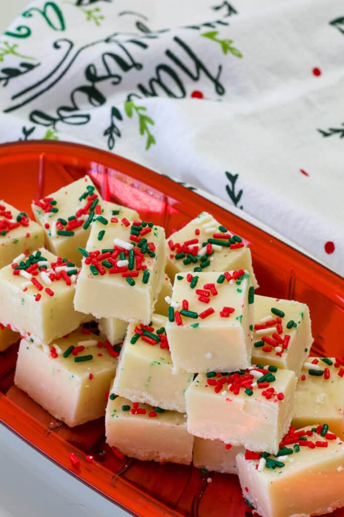 A shiny red platter with pieces of Sugar Cookie Christmas Fudge stacked on each other.