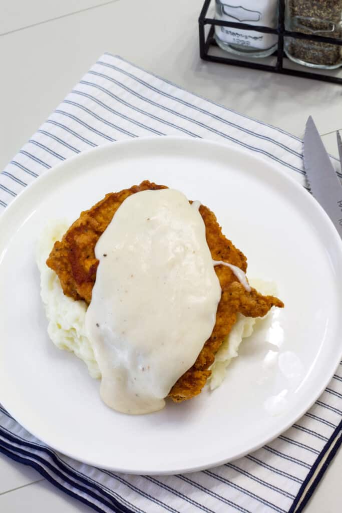 One fried pork chop on a bed of creamy mashed potatoes and topped with sawmill gravy.