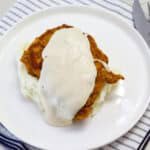 Overhead view of one pork chop on a bed of mashed potatoes covered with gravy.