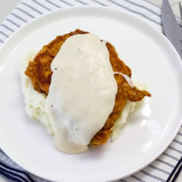 Overhead view of one pork chop on a bed of mashed potatoes covered with gravy.