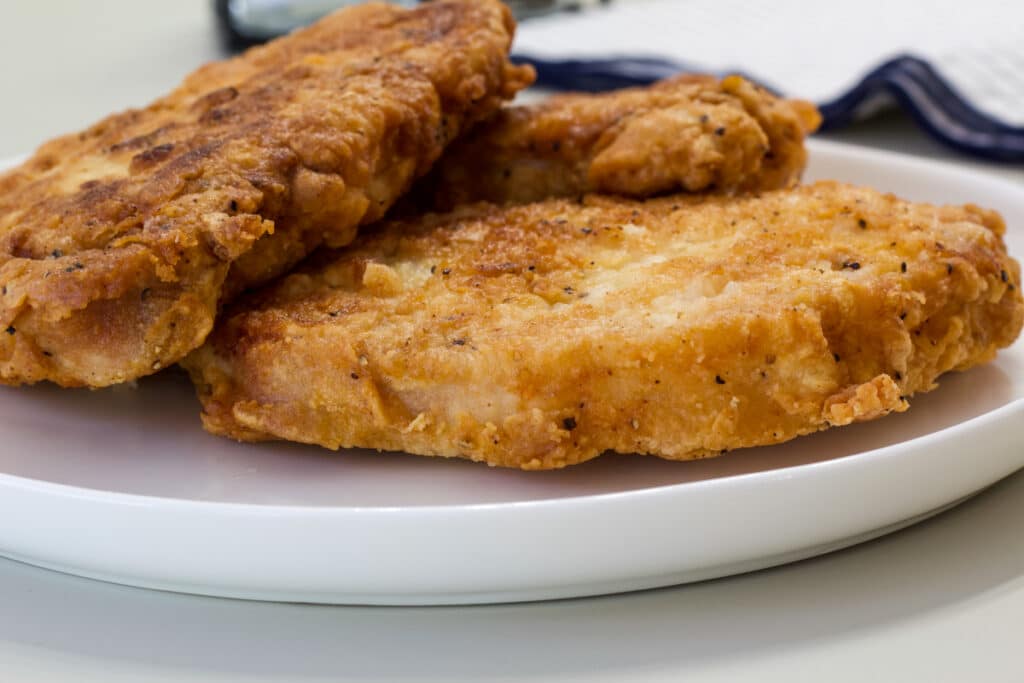Side view of three breaded and fried boneless pork chops on a plate.