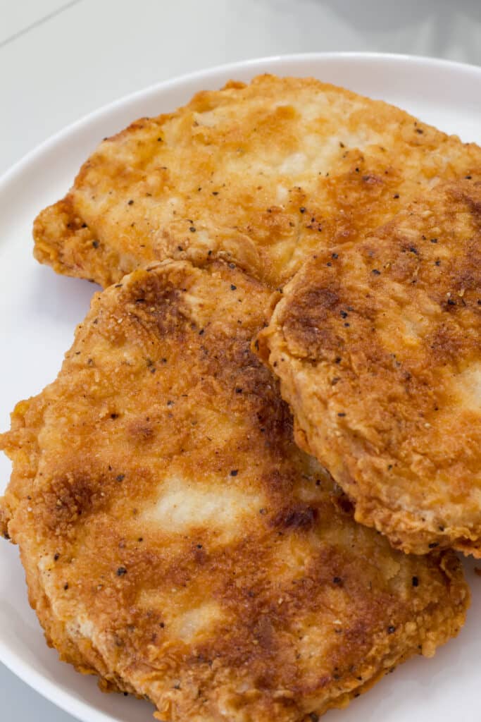 Three fried pork chops on a white plate.