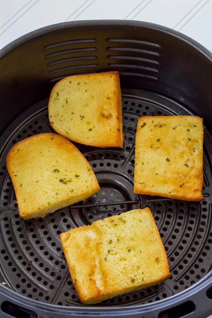Four pieces of air fried french style bread in the basket of the air fryer after they have been cooked.