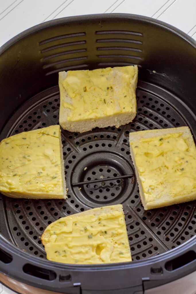 Four pieces of buttered bread in the air fryer basket before they have been air fried.