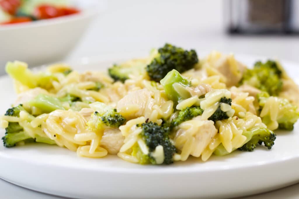 Side view of one serving of Cheesy Chicken & Broccoli Orzo on a white plate.