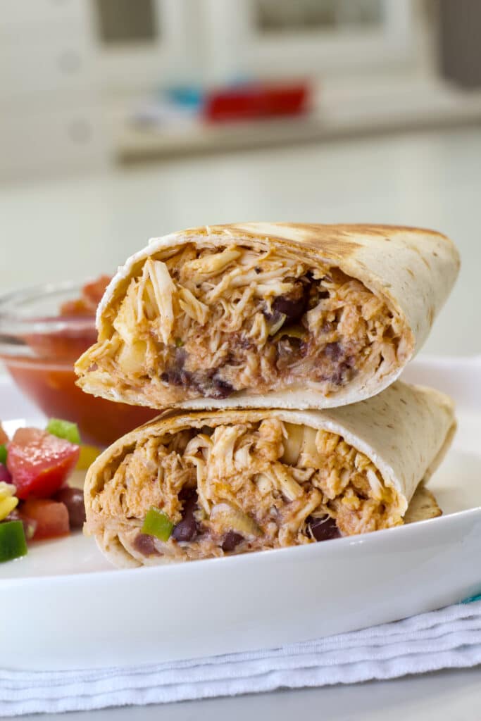 One Chicken and Black Bean Burrito on a plate split in half so the inside is visible.