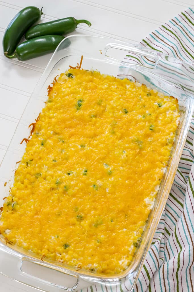 The whole baked Easy Jalapeno Cream Cheese Corn Casserole and three whole jalapenos to near the top left.
