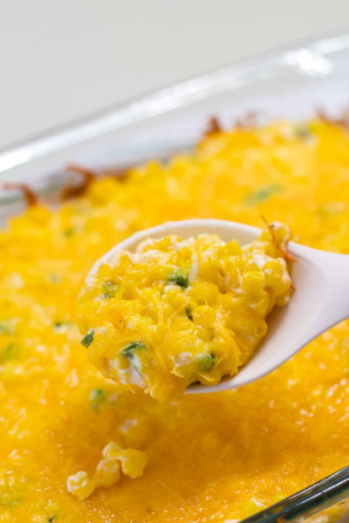 A spoonful of creamy cheddar corn casserole with the pan in the background.