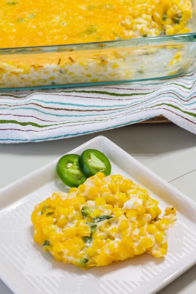 One serving of Easy Jalapeno Cream Cheese Corn Casserole on a plate with the rest of the casserole in the background.