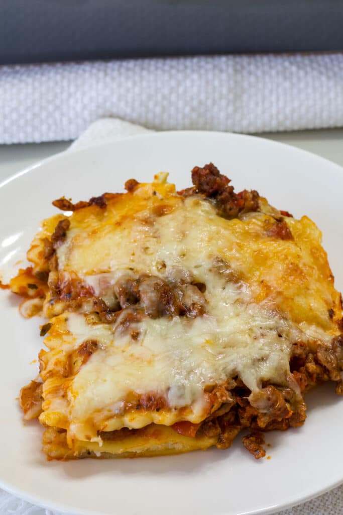 Side view of one serving of lasagna casserole on a white plate.