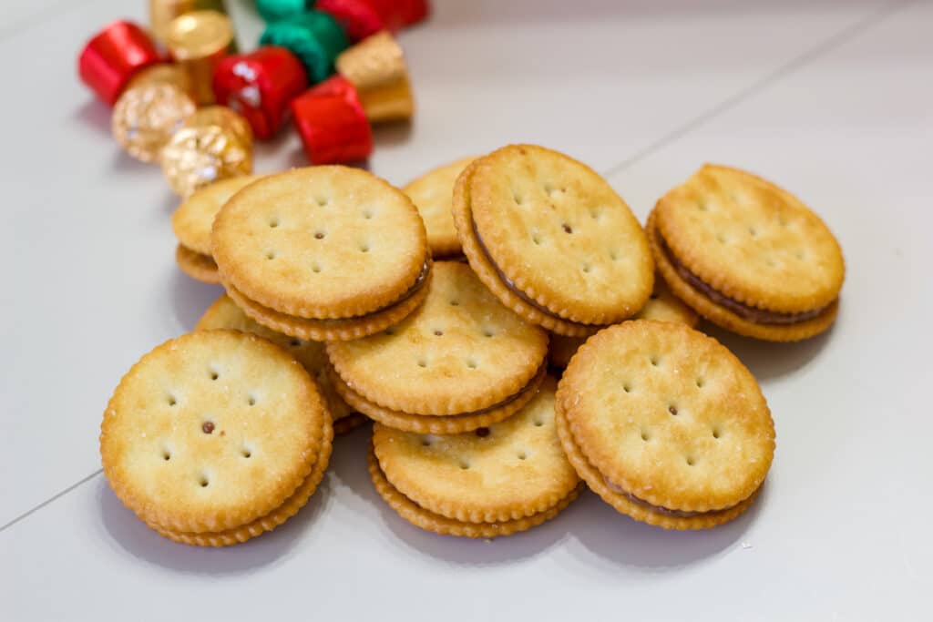 A pile of Easy Rolo Stuffed Ritz Crackers Treats in the foreground and a pile of rolo candies in the background.