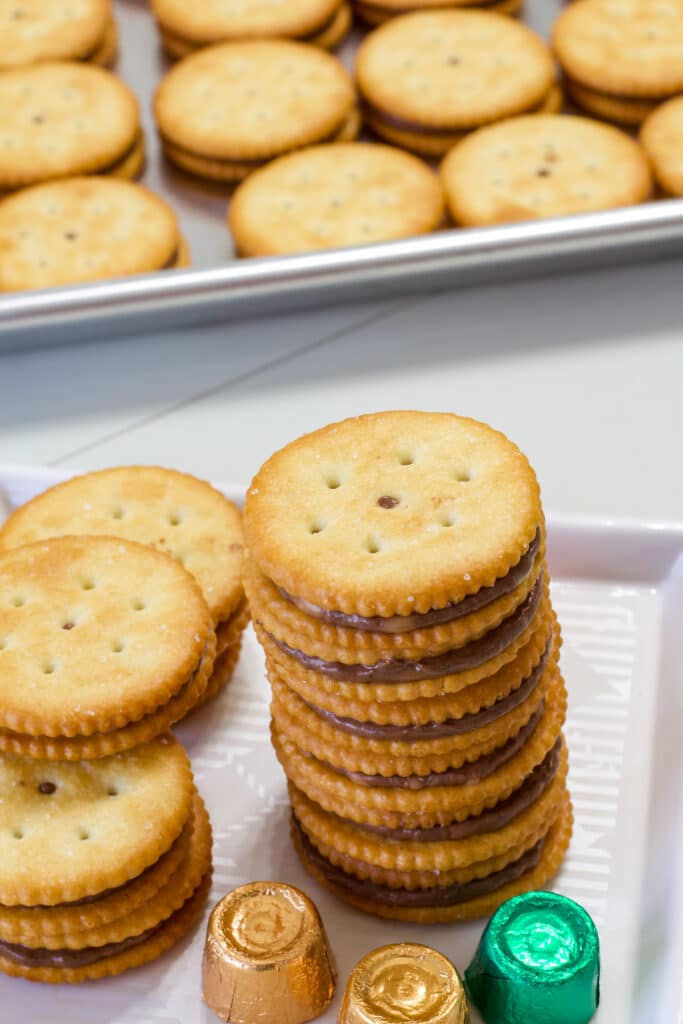 A stack of six rolo ritz cookies with some more around the stack and the sheet pan full of them in the background.