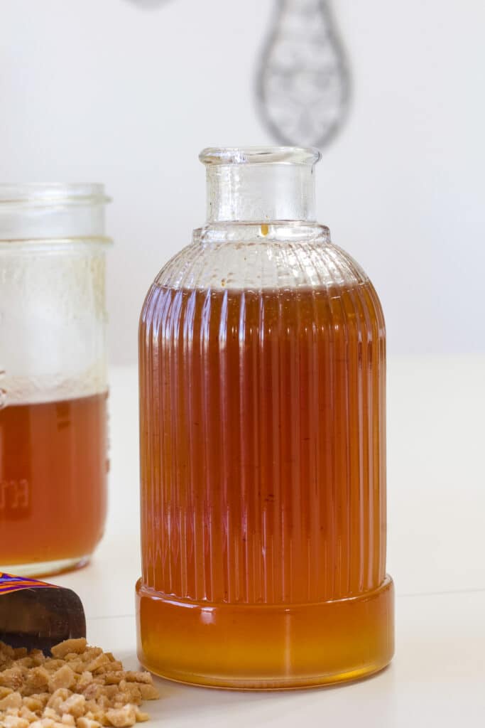 A pretty bottle filled with Homemade Toffee Nut Syrup and some heath bits beside it.