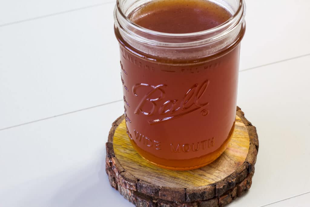 A mason jar sitting on a wooden coaster, it is full of Homemade Toffee Nut Syrup.