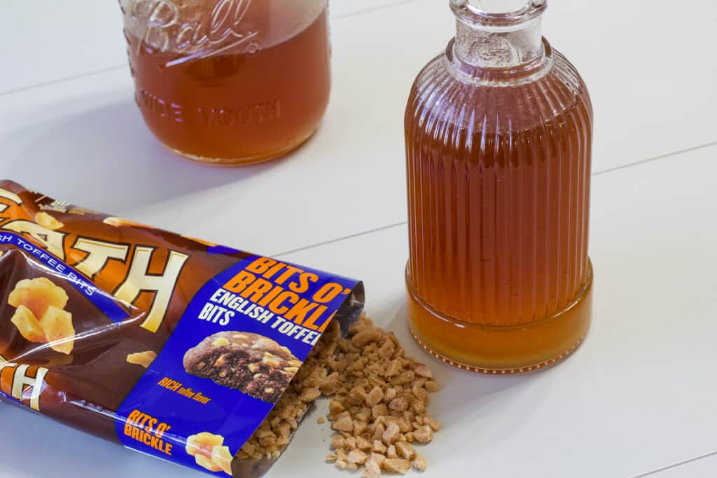 A mason jar and small bottle with toffee nut syrup in them and a bag of english toffee bits next to them.