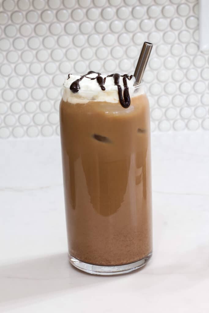 One tall glass of Iced Mocha Coffee topped with whipped cream and a chocolate sauce drizzle.