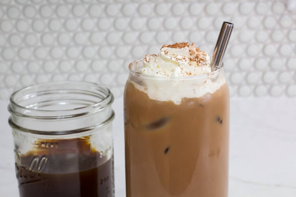 The top half of a glass of iced mocha coffee and a mason jar of coffee mixed with chocolate sauce next to it.