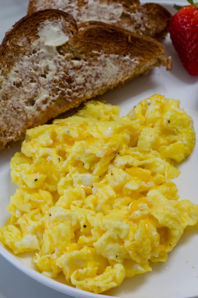 Cheesy scrambled eggs on a plate with berries and wheat toast.