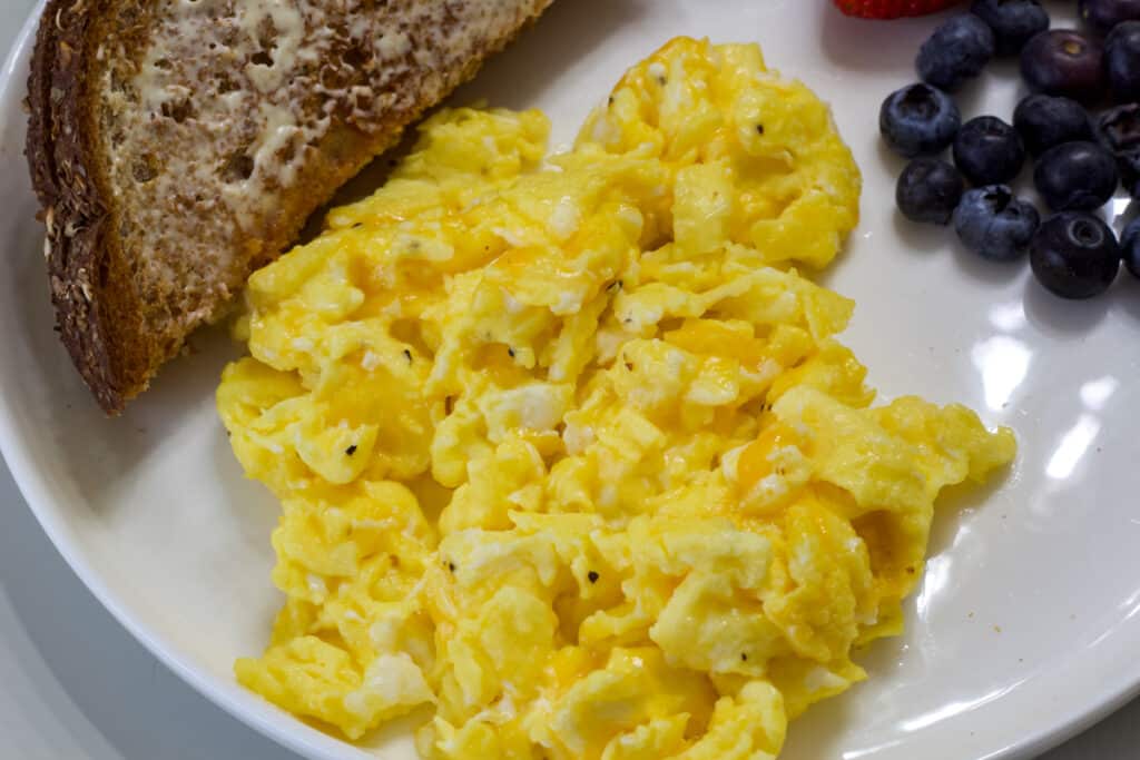Close up view of the cheesy scrambled eggs, part of the toast and berries are visible.