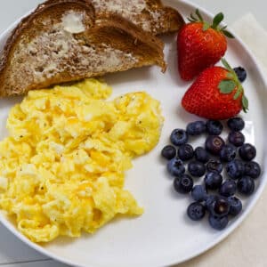 A plate with scrambled eggs with cheese, wheat toast, and fresh berries.