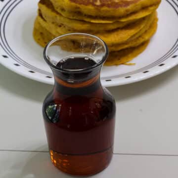 A bottle of 2 ingredient ihop copycat butter pecan syrup sitting in front of a stack of pumpkin pancakes.