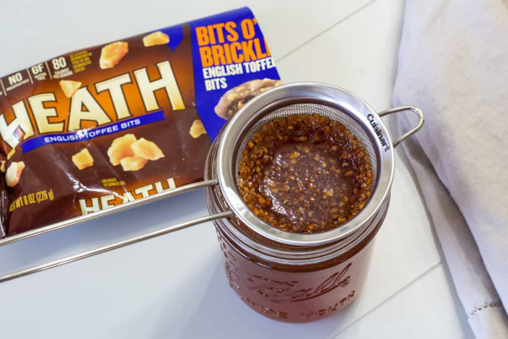 A mason jar with a small mesh strainer on top of it and the leftover toffee pieces are in it.