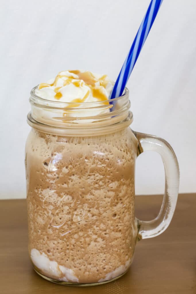 One mason jar mug with Copycat Starbucks Salted Caramel Mocha Frappuccino in it, there is a blue straw sticking out of it.