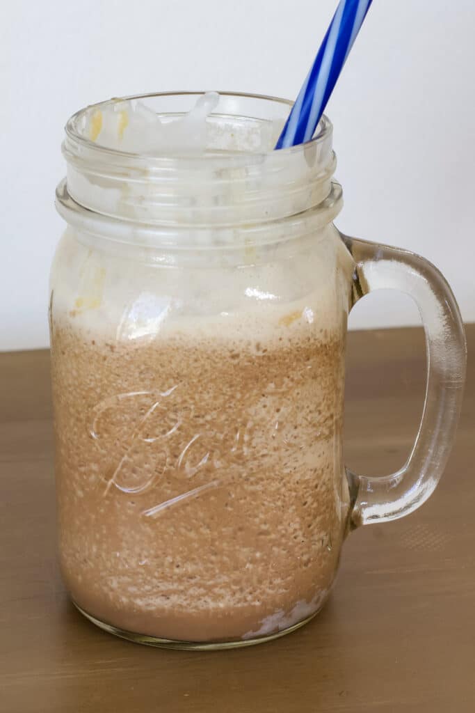 One glass mason jar mug that is three-fourths full of Salted Caramel Mocha Frappuccino with a blue straw in it.