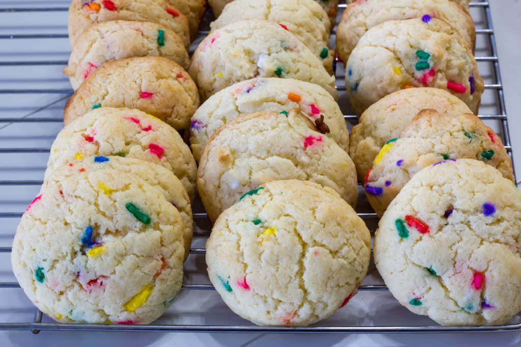 Many baked confetti cookies in rows on a silver wire cooling rack.