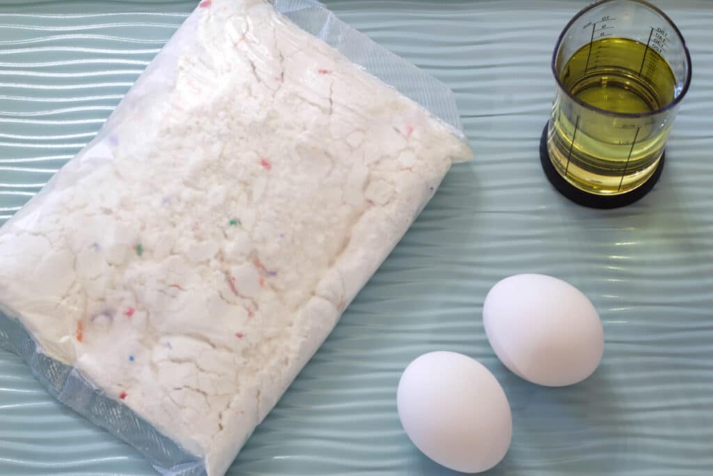 The cake mix, oil and eggs on a light green colored rimmed baking sheet.