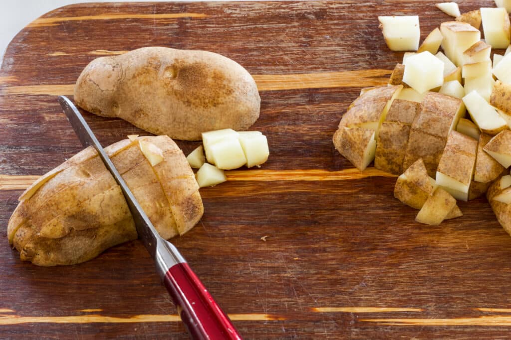 A completely cubed potato on the right and a potato being cut on the left.