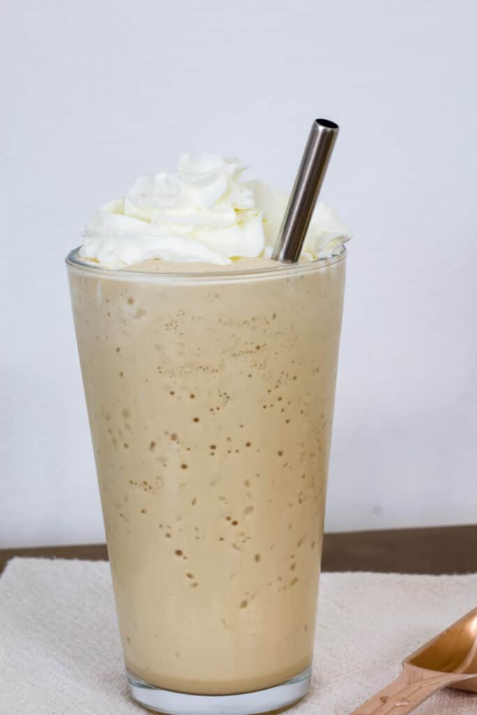One tall glass full of Starbucks Vanilla Frappuccino topped with whipped cream.