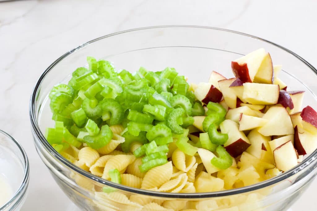 The pasta, celery, apples and walnuts in a glass bowl before being mixed.