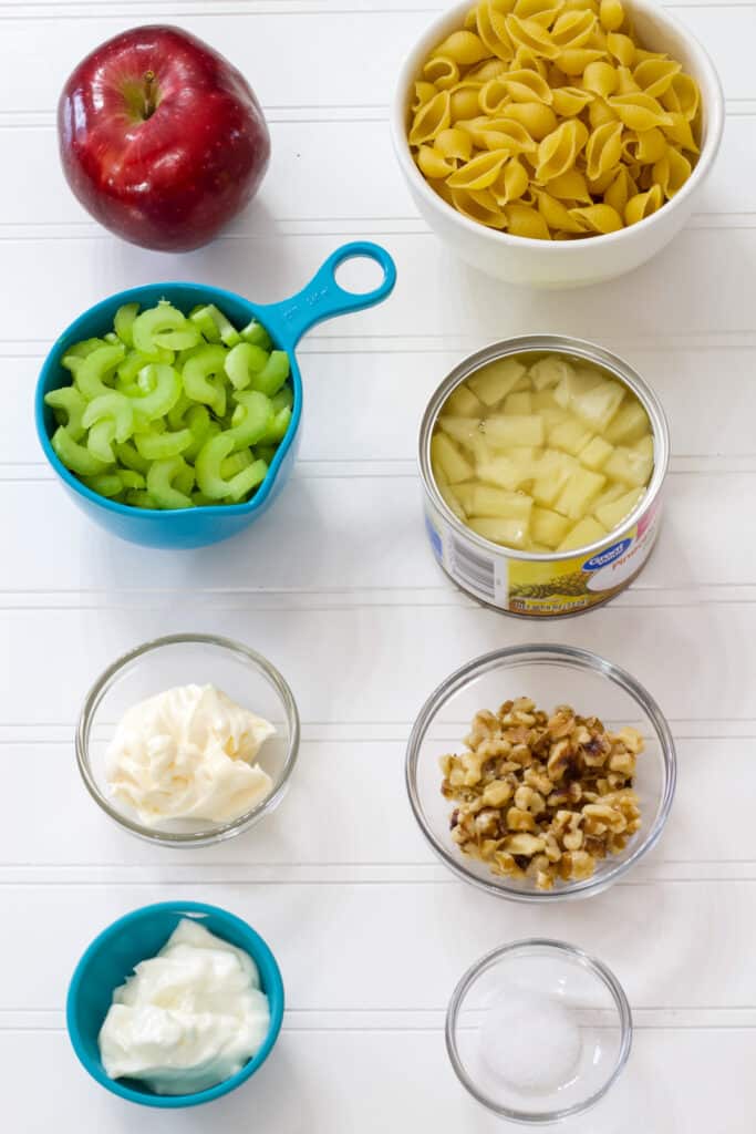 The apple, uncooked pasta, chopped celery, walnuts, sour cream, mayo, and salt measured out