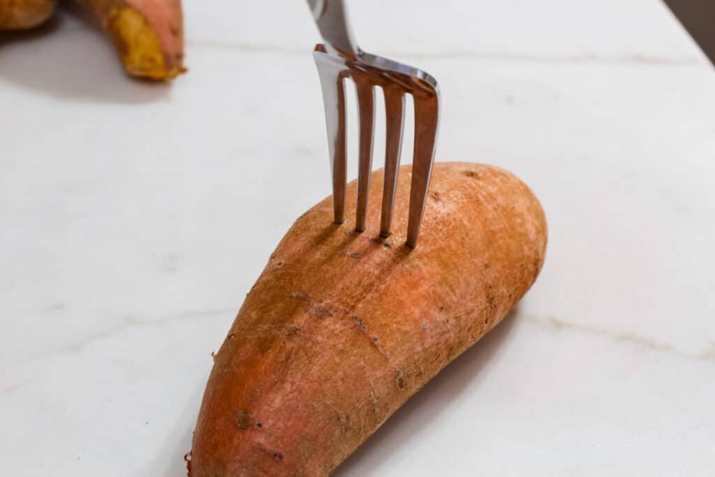 A fork sticking into a whole sweet potato.