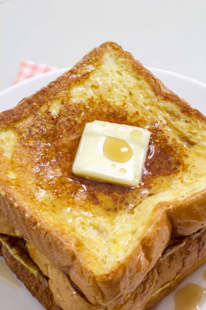 Close up overhead view of 3 slices of Texas toast french toast with a pat of butter and maple syrup on it.