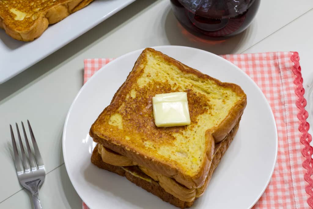 Overhead view of pieces of french toast on a white plate that is sitting on a pink and white checkered napkin.